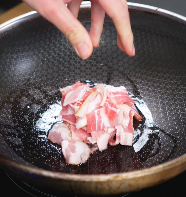 Strips of bacon sizzle in a hot pan, releasing their fat and turning golden brown for the smoky flavor base of the pasta.