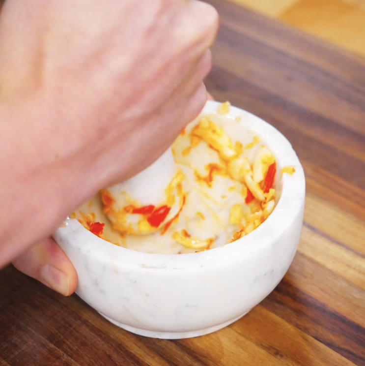 A marble mortar and pestle crush garlic and red Thai chilies into a fragrant paste that will form the base of this spicy fried rice.