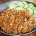 Sliced honey garlic chicken thighs served over a bowl of white rice with fresh cucumber slices on the side, showcasing the glossy, sticky glaze.