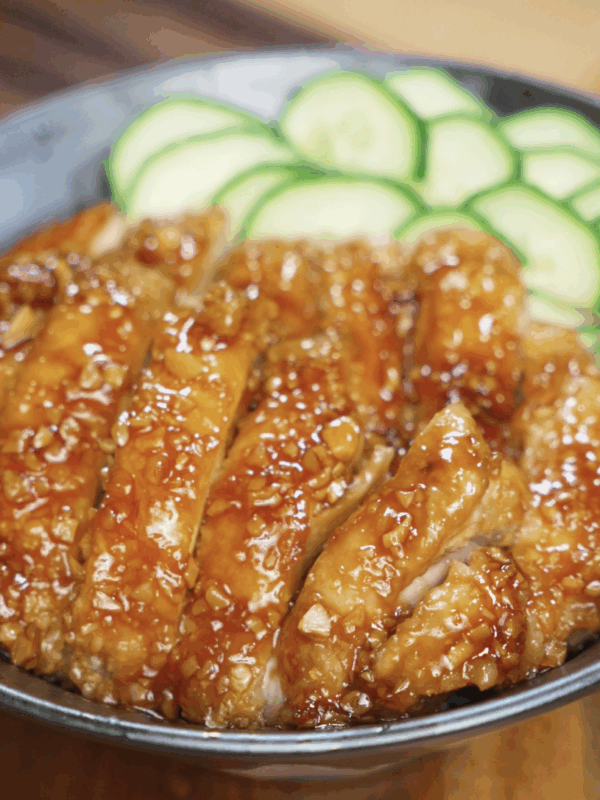 Sliced honey garlic chicken thighs served over a bowl of white rice with fresh cucumber slices on the side, showcasing the glossy, sticky glaze.
