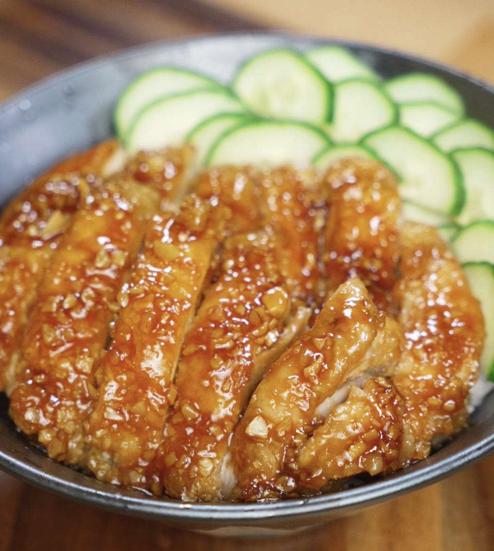 Sliced honey garlic chicken thighs served over a bowl of white rice with fresh cucumber slices on the side, showcasing the glossy, sticky glaze.