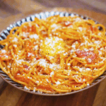 A plate of gochujang carbonara is topped with an egg yolk, parmesan, and freshly cracked black pepper for a rich, indulgent finish.