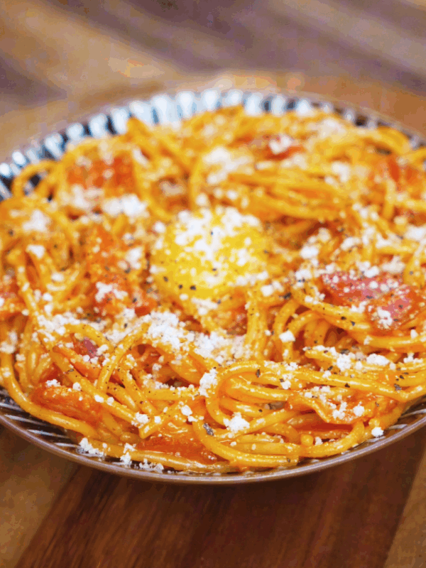 A plate of gochujang carbonara is topped with an egg yolk, parmesan, and freshly cracked black pepper for a rich, indulgent finish.