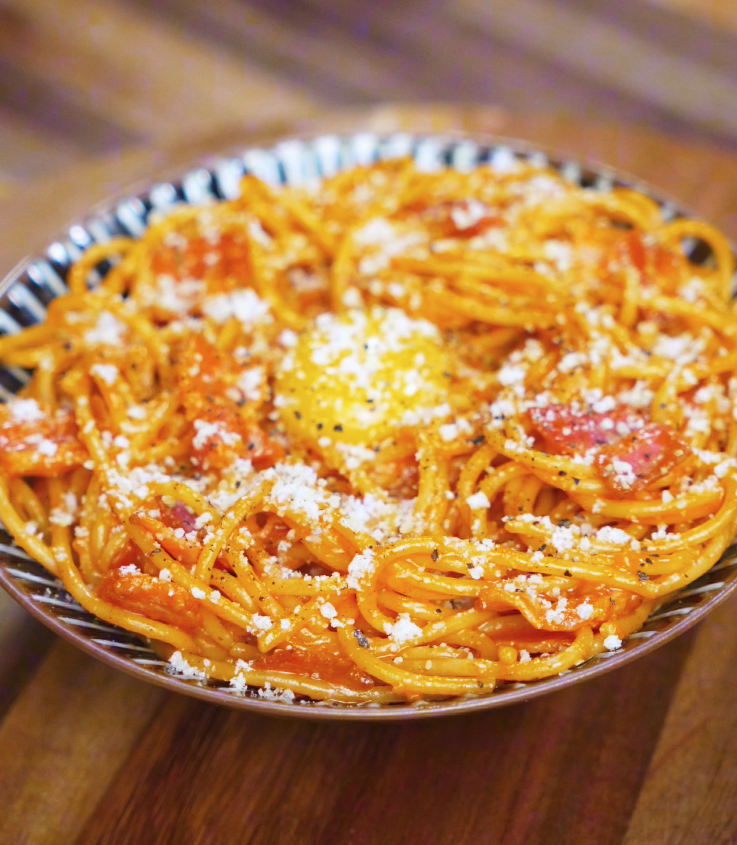 A plate of gochujang carbonara is topped with an egg yolk, parmesan, and freshly cracked black pepper for a rich, indulgent finish.