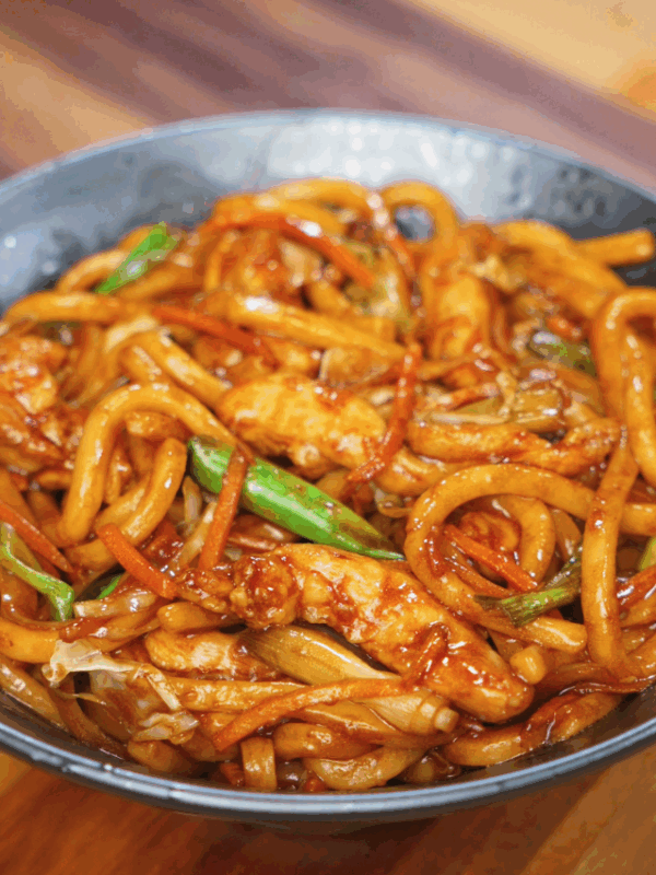 A full bowl of chicken yaki udon filled with glossy noodles, carrots, cabbage, and scallions coated in a rich soy-based stir-fry sauce.