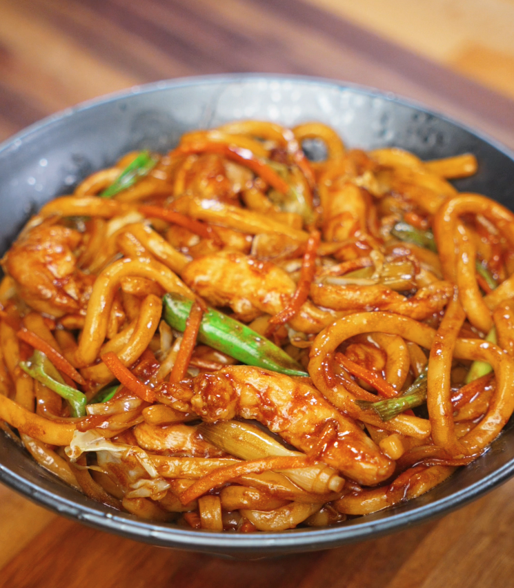 A full bowl of chicken yaki udon filled with glossy noodles, carrots, cabbage, and scallions coated in a rich soy-based stir-fry sauce.