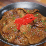 A full bowl of ginger pork served over white rice, topped with thin slices of glossy pork, caramelized onions, scallions, and pickled ginger.