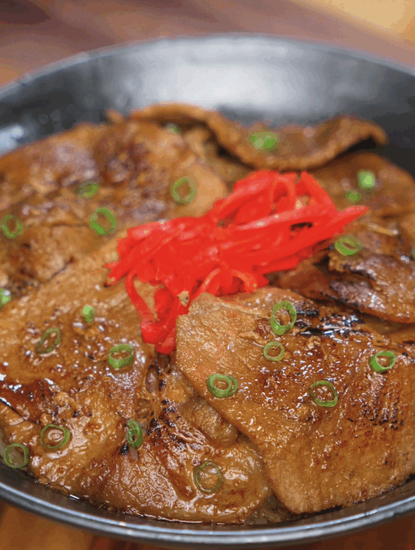 A full bowl of ginger pork served over white rice, topped with thin slices of glossy pork, caramelized onions, scallions, and pickled ginger.