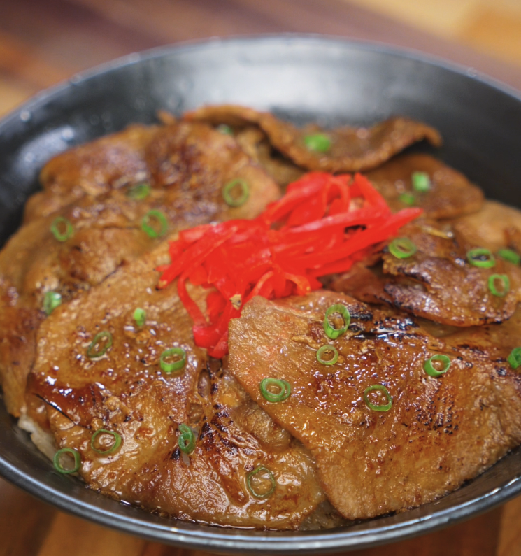 A full bowl of ginger pork served over white rice, topped with thin slices of glossy pork, caramelized onions, scallions, and pickled ginger.