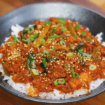 A full bowl of spicy pork bulgogi served over white rice, topped with caramelized pork, tender scallions, and a sprinkle of sesame seeds.