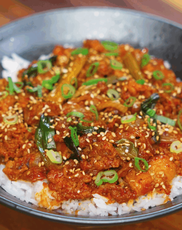 A full bowl of spicy pork bulgogi served over white rice, topped with caramelized pork, tender scallions, and a sprinkle of sesame seeds.
