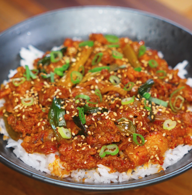 A full bowl of spicy pork bulgogi served over white rice, topped with caramelized pork, tender scallions, and a sprinkle of sesame seeds.