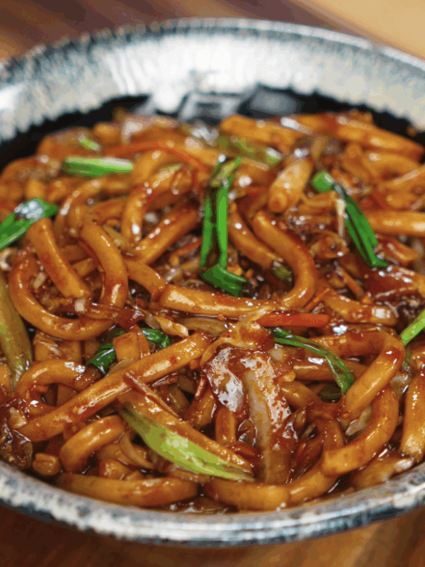 A bowl of glossy teriyaki udon noodles mixed with sautéed cabbage, carrots, garlic, and scallions, coated in a rich, savory-sweet sauce.