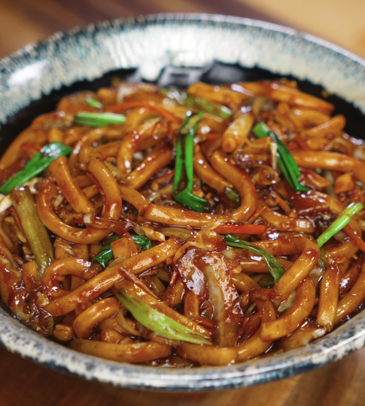 A bowl of glossy teriyaki udon noodles mixed with sautéed cabbage, carrots, garlic, and scallions, coated in a rich, savory-sweet sauce.