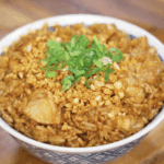 A full bowl of garlic chicken fried rice topped with scallions and crispy garlic sits ready to eat, showcasing caramelized chicken and perfectly seasoned rice.
