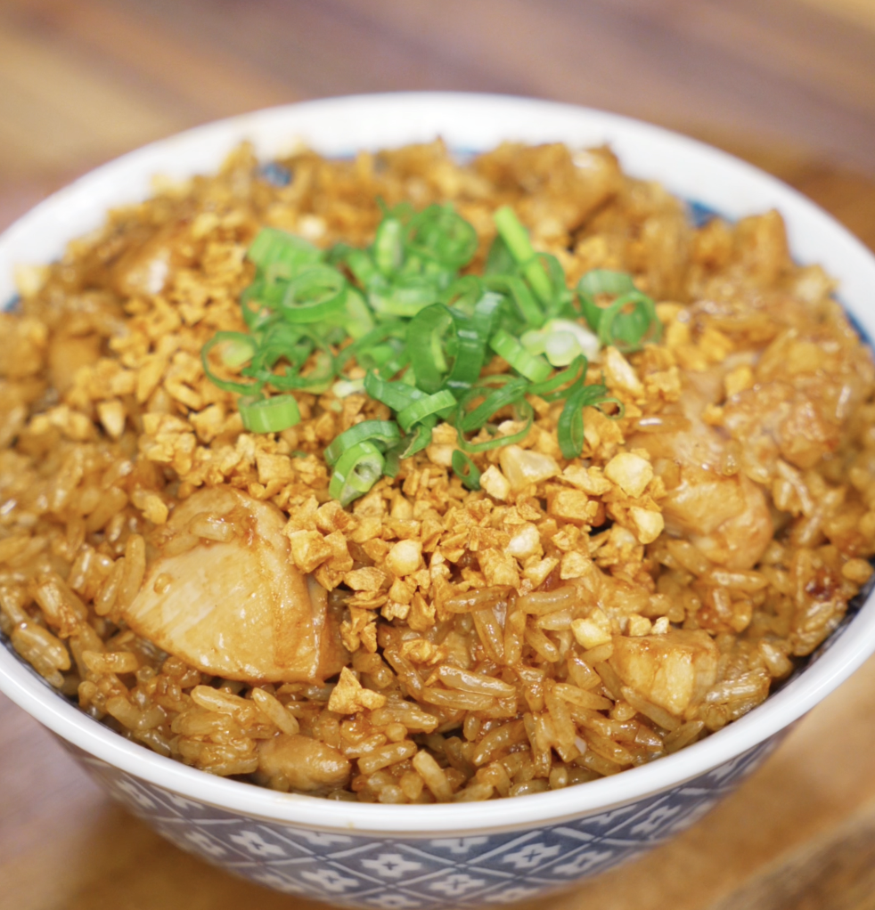 A full bowl of garlic chicken fried rice topped with scallions and crispy garlic sits ready to eat, showcasing caramelized chicken and perfectly seasoned rice.