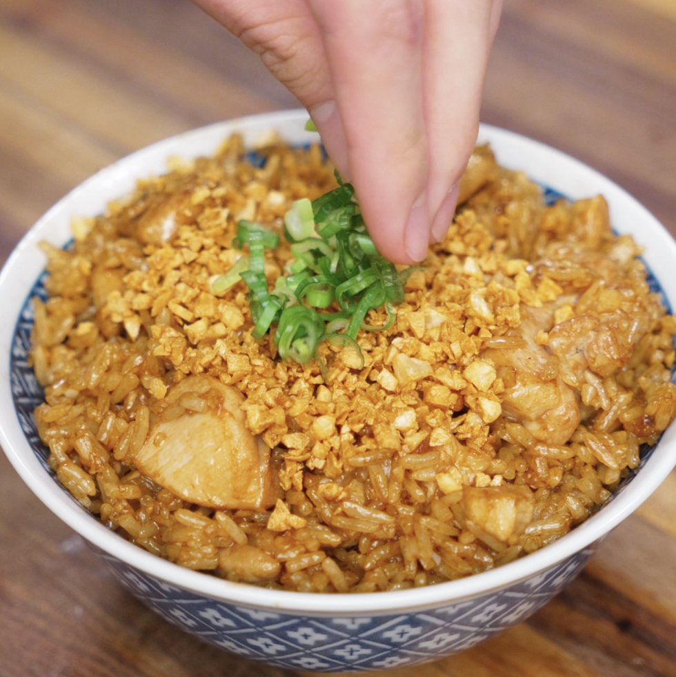 Freshly sliced scallions are sprinkled on top of a bowl of garlic chicken fried rice, already loaded with crispy garlic bits.