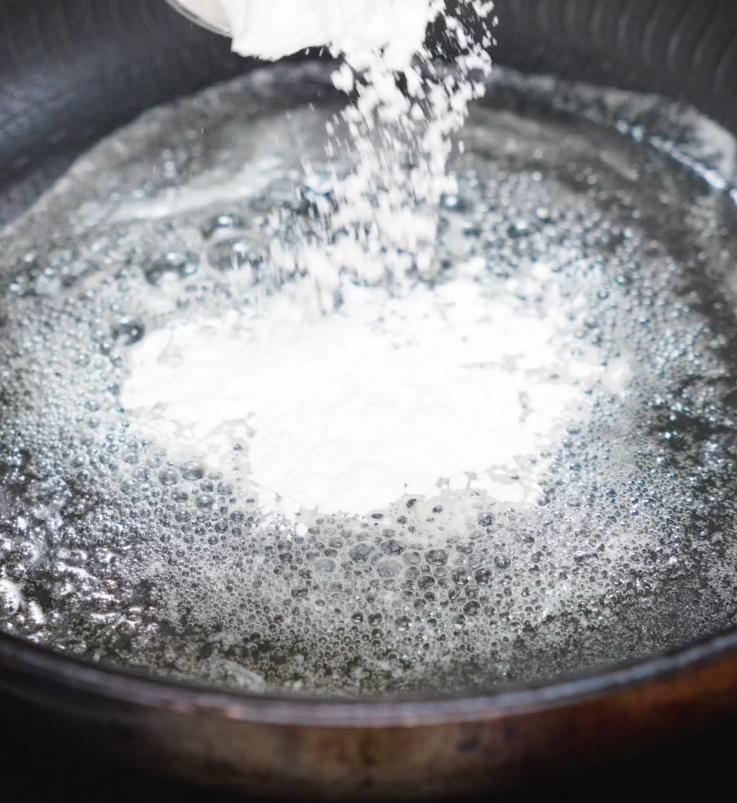 Flour is sprinkled into melted butter in a hot pan, sizzling as it forms the base of the creamy cheese sauce.