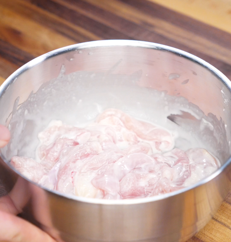 Sliced chicken thighs marinate in a bowl with shaoxing wine, cornstarch, and salt, creating a silky texture for stir-frying.