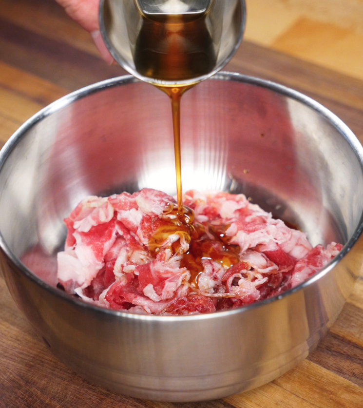 Soy sauce is poured over a bowl of thinly sliced beef, combining with garlic and seasonings for a quick marinade.