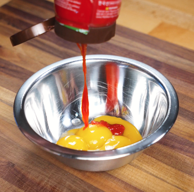 A squeeze of gochujang is added to egg yolks in a metal bowl, creating the rich, spicy foundation for the carbonara sauce.