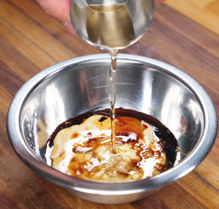 Vinegar is poured into a bowl of peanut butter, sesame paste, soy sauce, and aromatics, forming the rich base for the noodle sauce.