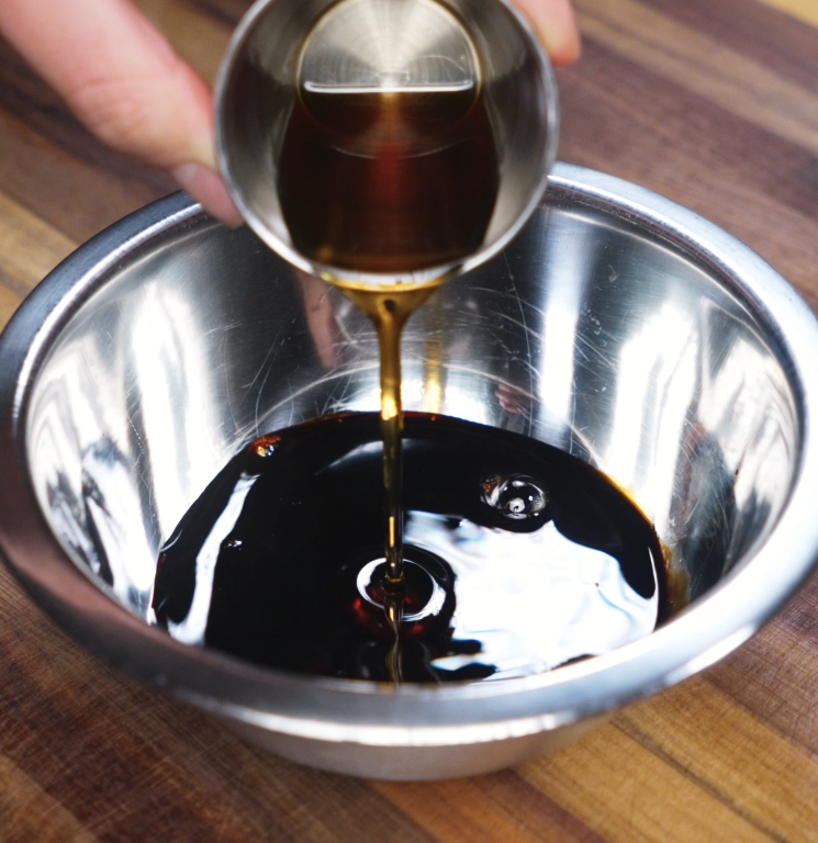 Soy sauce is poured into a metal mixing bowl with sesame oil and other ingredients to create a rich teriyaki stir fry sauce.