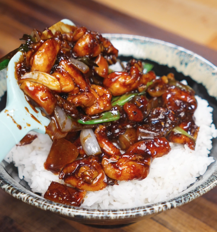 A spoonful of black pepper chicken is served over steaming white rice, with the sauce soaking into each grain for a bold and savory finish.
