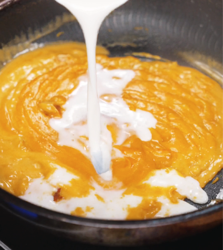 Smooth milk is poured into a pan of melted gochujang and roux, blending into a rich orange base that will become the creamy cheese sauce.