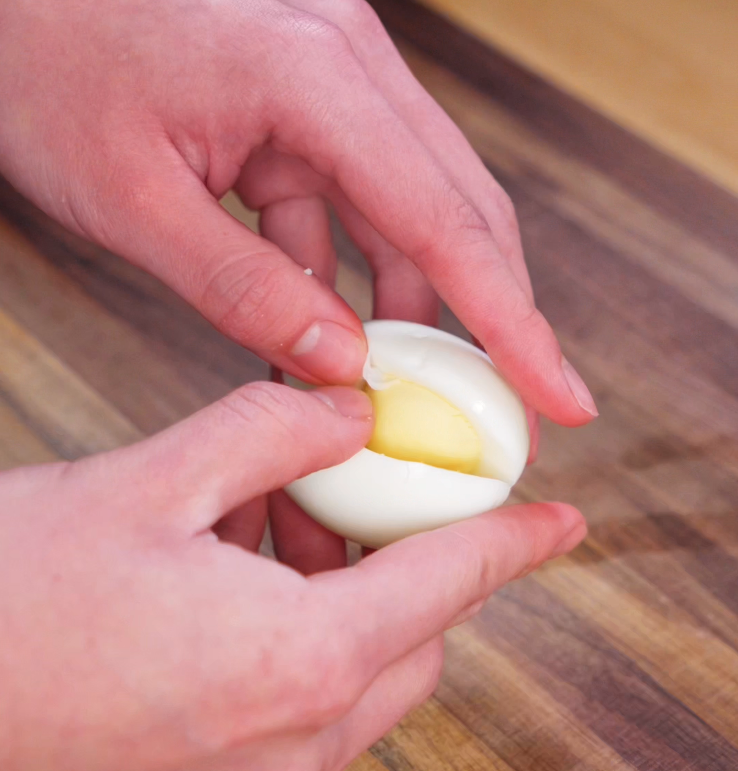 A hard-boiled egg is gently pulled apart by hand to separate the yolk, which will be mashed into the spicy deviled egg filling.