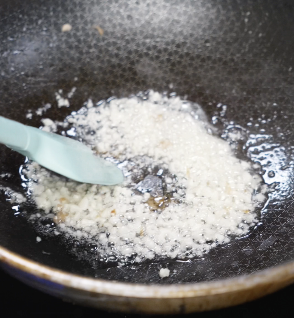 Finely minced garlic is being sautéed in oil in a hot nonstick pan, bubbling gently as it becomes fragrant and golden.
