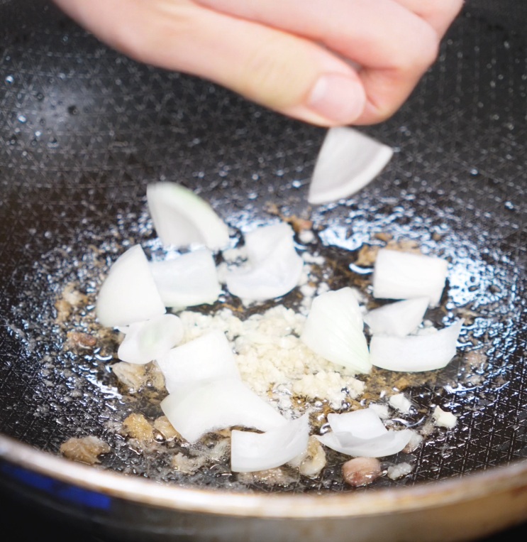 Chopped garlic and onion wedges are added to the hot pan after browning the chicken to build the aromatic foundation of the dish.