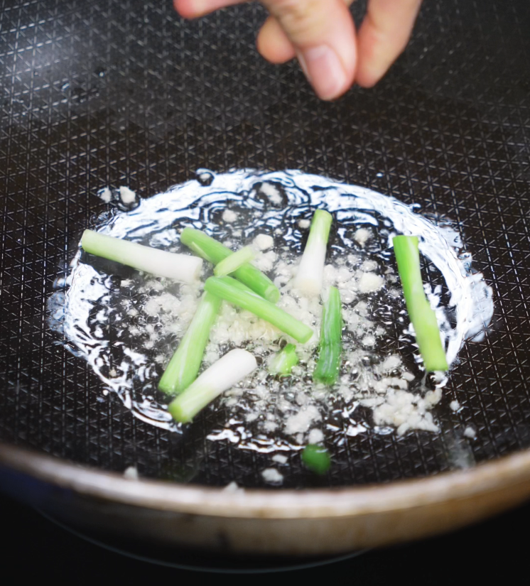 Chopped scallion whites and finely minced garlic sizzle in hot oil, filling the pan with aroma as the stir fry base cooks.