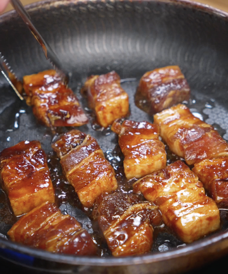 Pork belly pieces sizzle in a hot skillet, forming a deep brown crust as the glaze thickens and caramelizes around each bite.