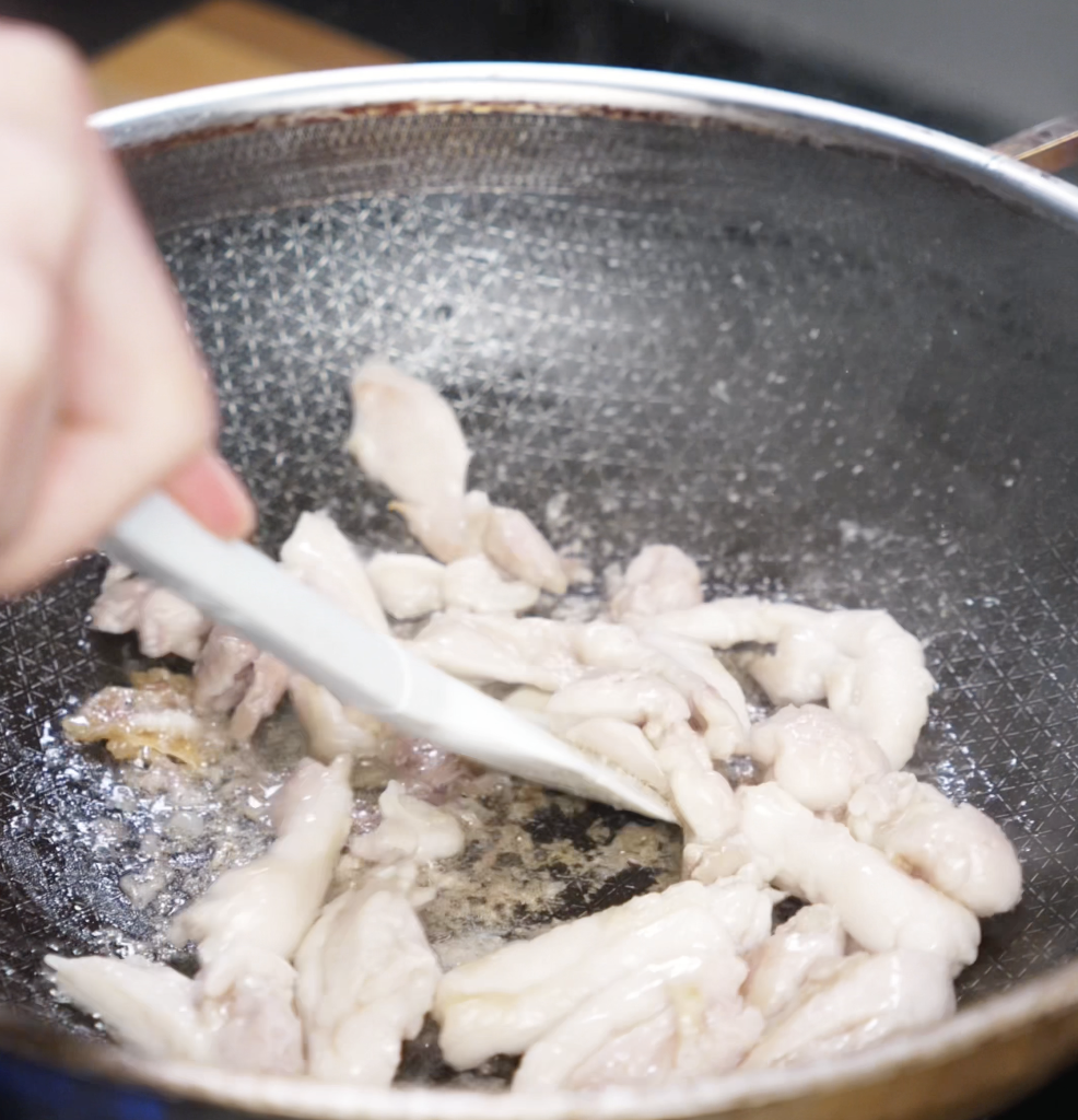Thinly sliced chicken thighs are being seared in a hot wok until golden brown. This builds savory depth and texture for the noodle stir-fry.