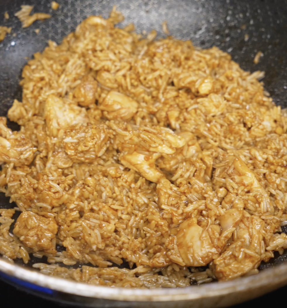 Chicken and rice are stir-fried together in the pan, evenly coated with a savory soy-based sauce for a rich, golden color.