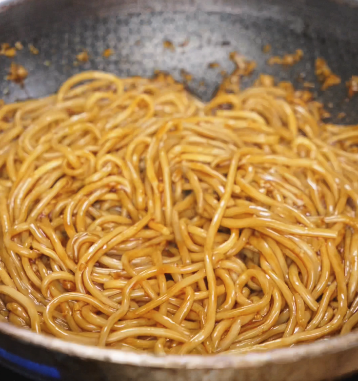 Cooked noodles are returned to the pan and tossed in the glossy garlic sauce, soaking up every drop.
