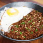 Finished honey garlic beef rice bowl topped with scallions and sesame seeds, served with a sunny-side-up egg over fluffy white rice.