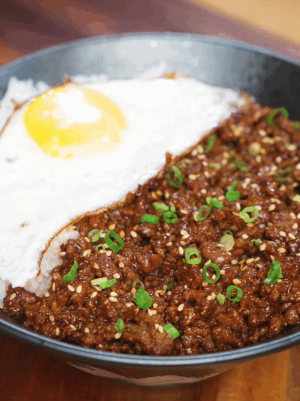 Finished honey garlic beef rice bowl topped with scallions and sesame seeds, served with a sunny-side-up egg over fluffy white rice.