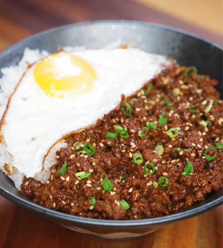 Finished honey garlic beef rice bowl topped with scallions and sesame seeds, served with a sunny-side-up egg over fluffy white rice.
