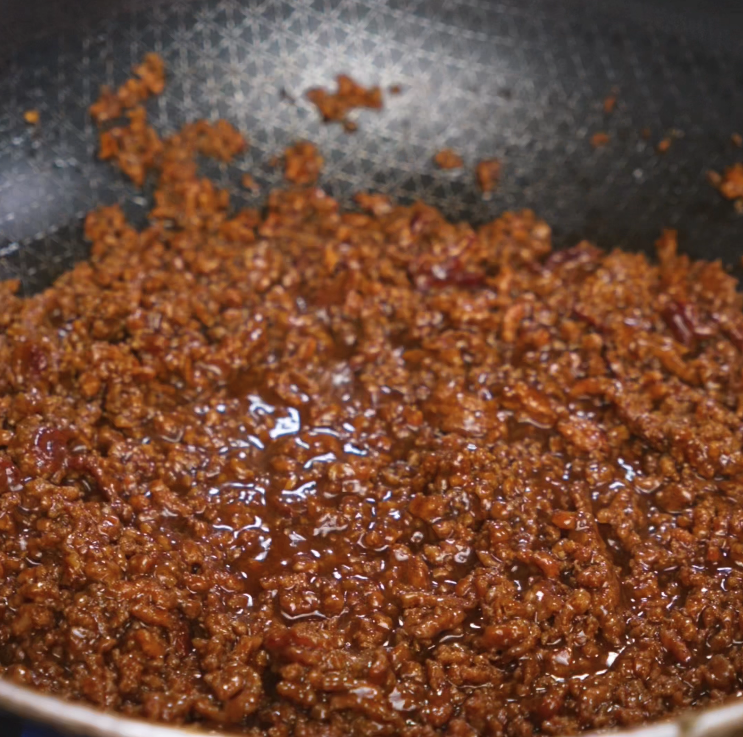 Simmering honey garlic beef in a skillet until thickened and glossy. The sauce has reduced and clings tightly to the ground beef, intensifying the flavor.