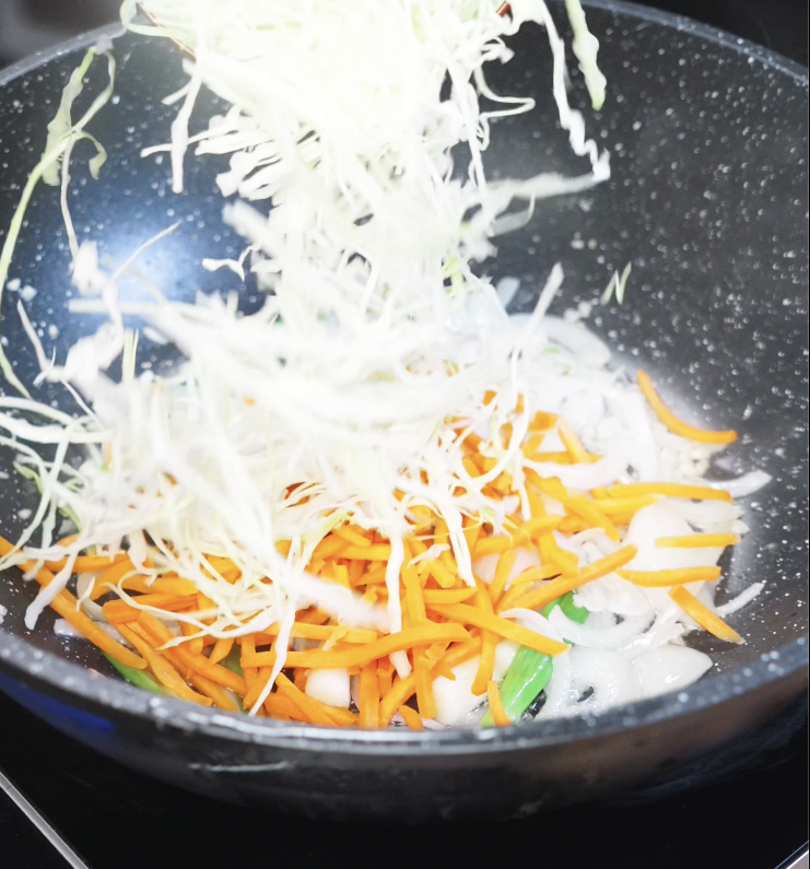 Shredded cabbage and carrots are tossed into the pan with aromatics to complete the veggie stir-fry base.