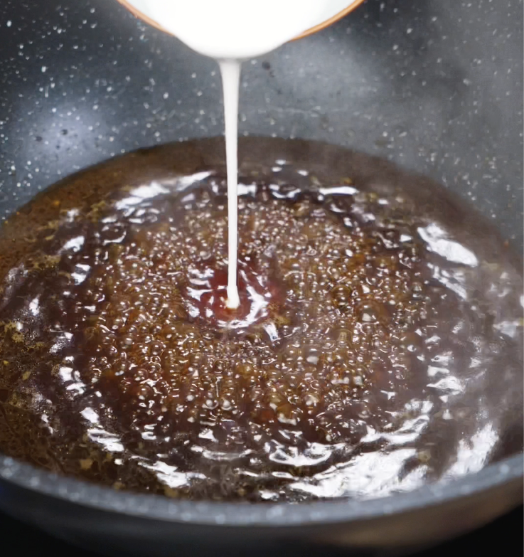 A cornstarch slurry being poured into the simmering sauce to thicken it.