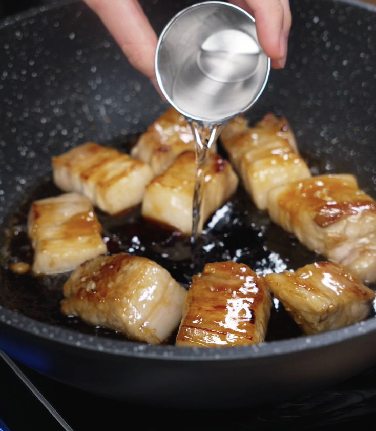 Shaoxing wine is poured into the pan of seared pork belly to deglaze and build a rich, savory braising liquid.