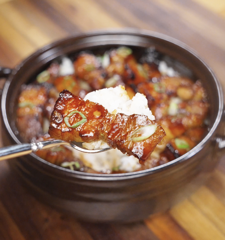A close-up shot of a single air-fried pork belly piece held over a bowl of white rice, showing crispy edges and sticky glaze.