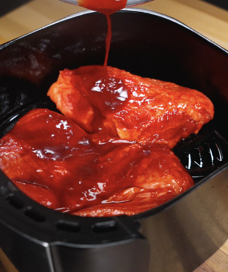 Marinated pork pieces placed in the air fryer basket while extra marinade is poured on top.