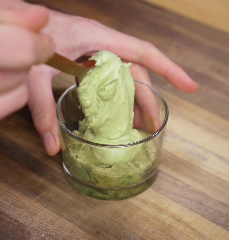 Whipped matcha cream is spooned into a glass over soaked ladyfingers, beginning the first layer of tiramisu.