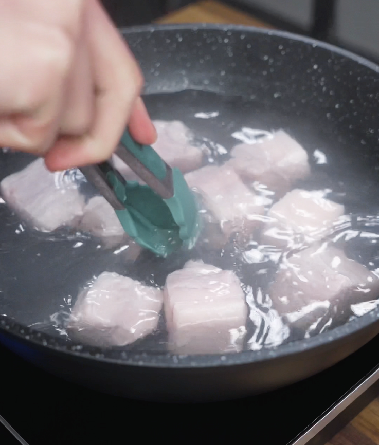 Cubes of pork belly are simmered in boiling water to remove impurities before caramelizing.