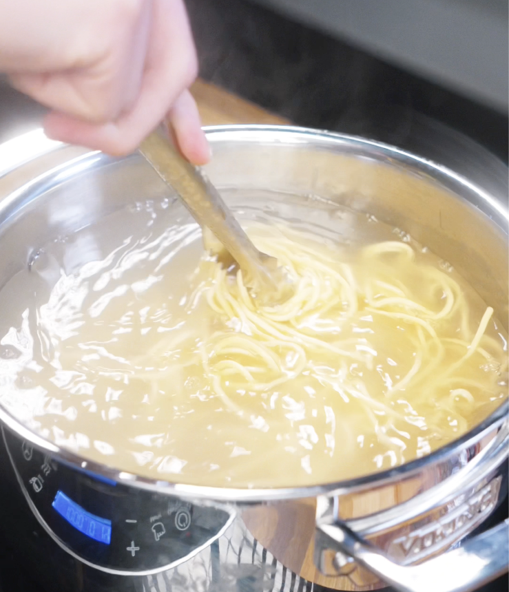 Noodles are cooking in a pot of boiling water just before being drained for stir-frying.