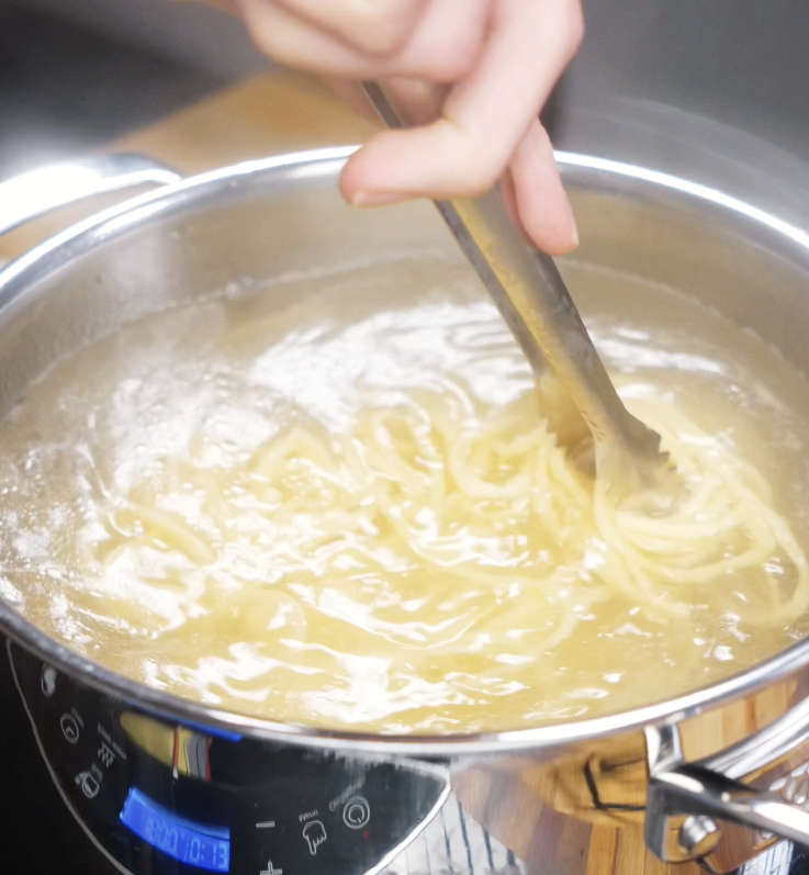 Noodles are stirred in a pot of boiling water with tongs until just before al dente.